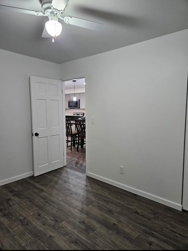 spare room featuring baseboards, dark wood-style flooring, and ceiling fan