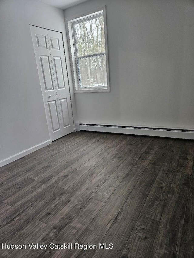 spare room with a baseboard heating unit, dark wood finished floors, and baseboards