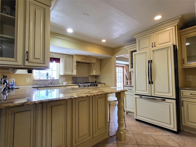 kitchen featuring light tile patterned flooring, paneled built in refrigerator, stove, cream cabinetry, and light stone countertops