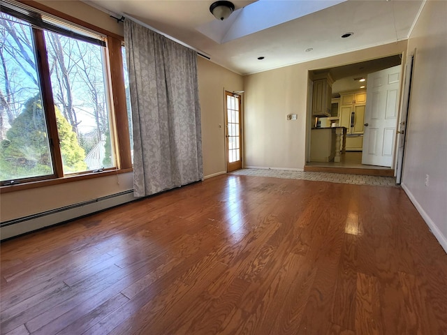 unfurnished room featuring a healthy amount of sunlight, baseboards, baseboard heating, and wood finished floors