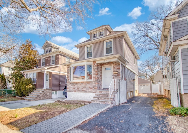 american foursquare style home featuring a garage, stone siding, and an outdoor structure