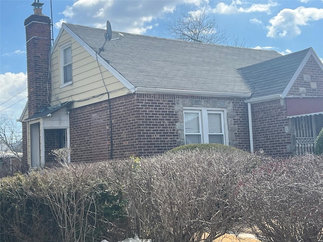 exterior space with brick siding, a chimney, and roof with shingles