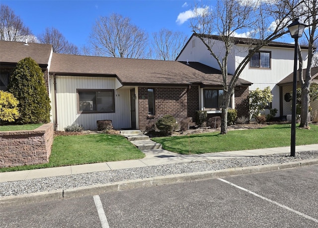 view of front of home featuring a shingled roof, uncovered parking, a front lawn, and brick siding