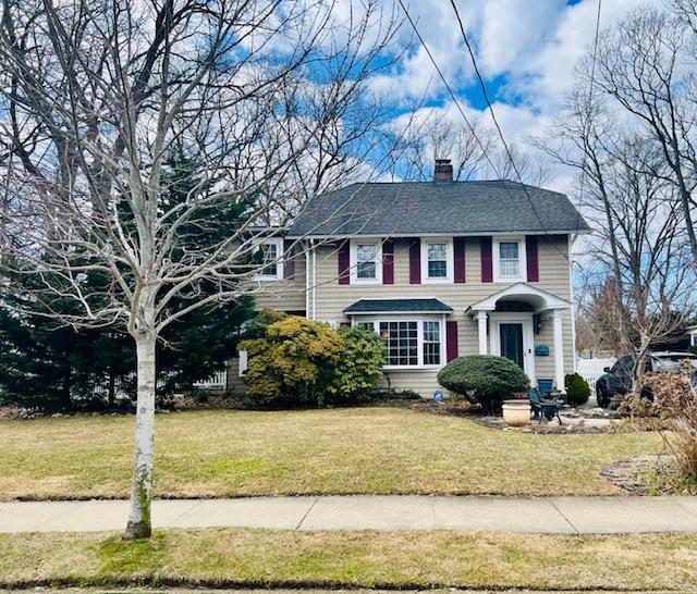 view of front of home featuring a chimney, a front lawn, and roof with shingles