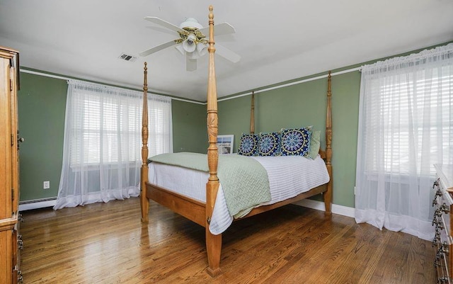 bedroom featuring a baseboard heating unit, wood finished floors, visible vents, and multiple windows