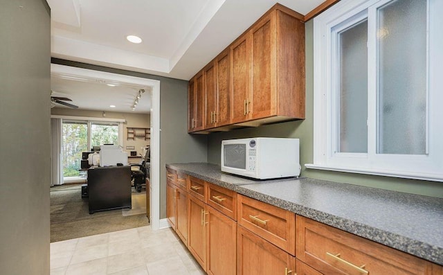 kitchen with ceiling fan, white microwave, light carpet, brown cabinets, and dark countertops