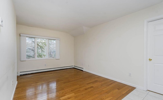 spare room featuring a baseboard radiator, baseboards, lofted ceiling, and light wood finished floors