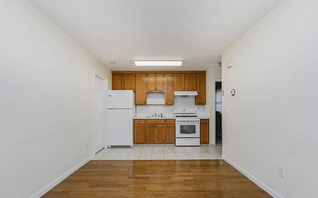 kitchen featuring white appliances, under cabinet range hood, light countertops, and light wood-style floors