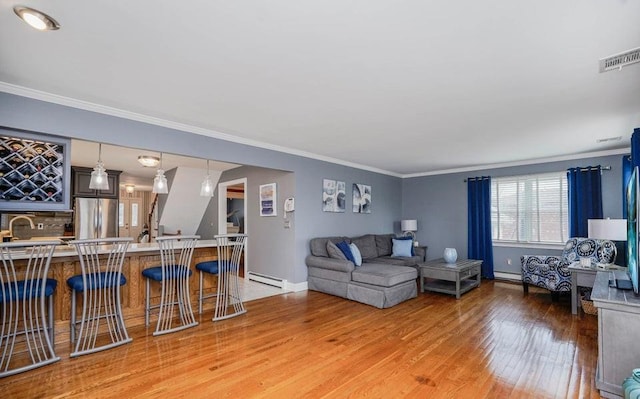 living room featuring visible vents, baseboards, light wood-style flooring, ornamental molding, and baseboard heating