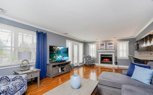 living area featuring light wood finished floors, a lit fireplace, visible vents, and crown molding