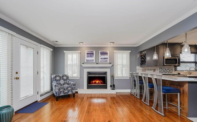 kitchen featuring light countertops, ornamental molding, light wood-type flooring, stainless steel microwave, and a kitchen bar