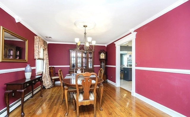 dining space featuring crown molding, a notable chandelier, visible vents, wood finished floors, and baseboards