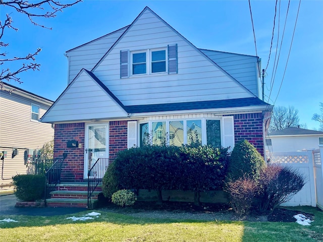 bungalow-style home with brick siding, a front lawn, a shingled roof, and fence