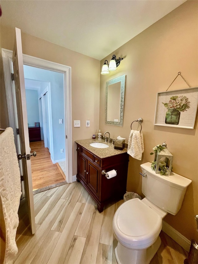 half bath with toilet, baseboards, wood finished floors, and vanity