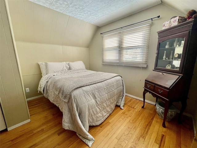 bedroom featuring wooden walls, baseboards, vaulted ceiling, and wood finished floors