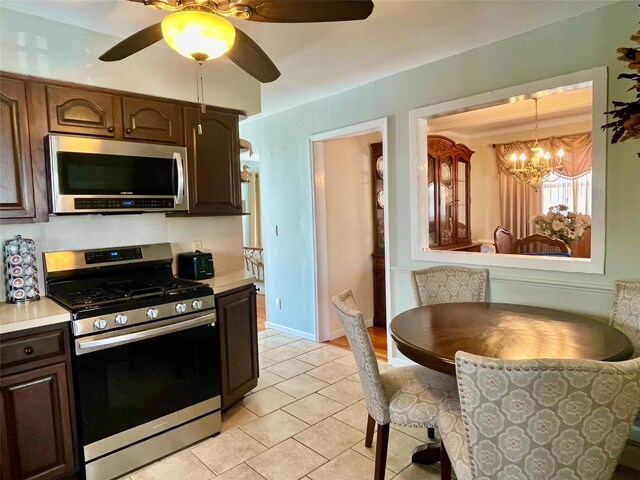 kitchen featuring stainless steel appliances, dark brown cabinets, ceiling fan with notable chandelier, light countertops, and light tile patterned floors