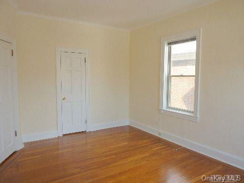 spare room with baseboards, wood finished floors, and ornamental molding