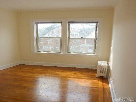 empty room featuring radiator heating unit, baseboards, a wealth of natural light, and wood finished floors