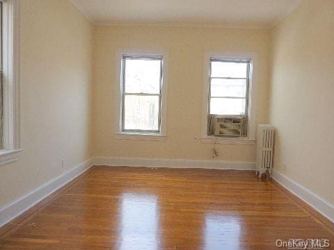 empty room with radiator, baseboards, and wood finished floors