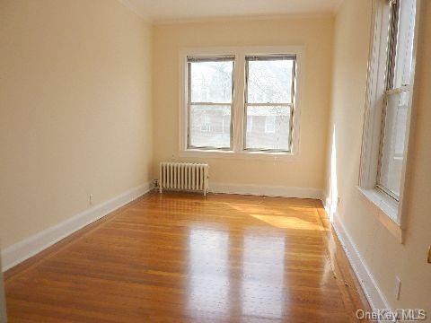 empty room with ornamental molding, radiator heating unit, wood finished floors, and baseboards