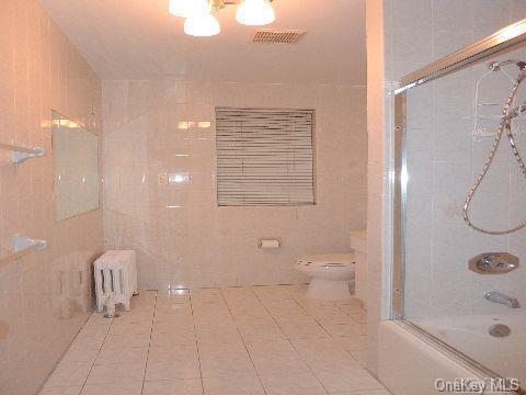 bathroom featuring enclosed tub / shower combo, tile walls, toilet, and tile patterned floors