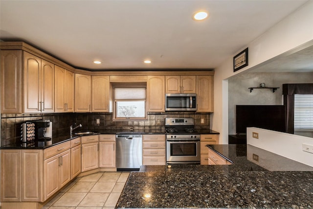 kitchen featuring light brown cabinets, a sink, dark stone countertops, stainless steel appliances, and decorative backsplash