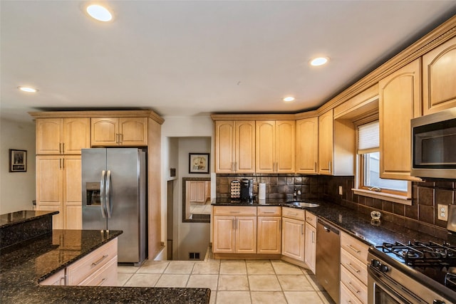 kitchen featuring light brown cabinets, a sink, dark stone countertops, stainless steel appliances, and light tile patterned floors