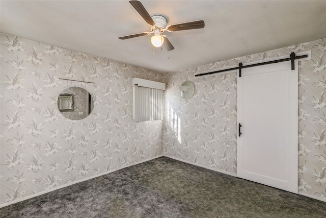 empty room featuring a barn door, wallpapered walls, a ceiling fan, and dark colored carpet