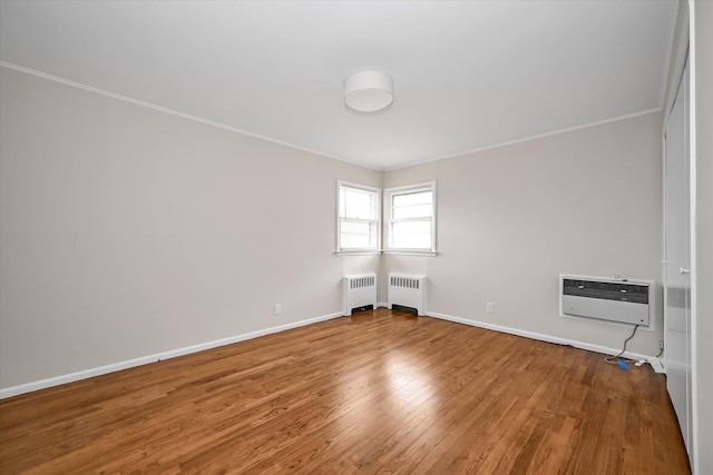 unfurnished room with radiator, wood finished floors, baseboards, and a wall mounted AC