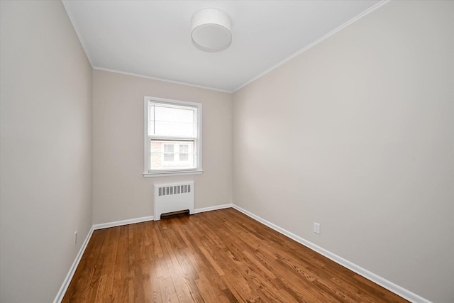 unfurnished room featuring baseboards, wood finished floors, radiator heating unit, and crown molding