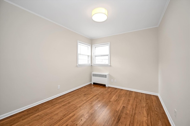 spare room with baseboards, radiator, wood finished floors, and ornamental molding