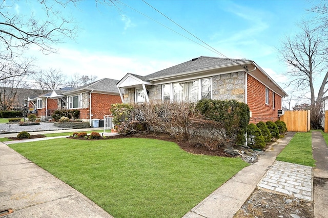 view of front facade with a front yard, fence, a shingled roof, stone siding, and brick siding