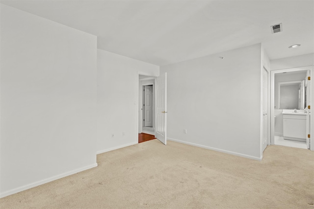 empty room featuring light carpet, visible vents, baseboards, and a sink