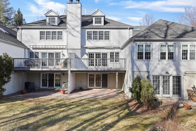 back of property with a lawn, french doors, a chimney, a deck, and a patio area