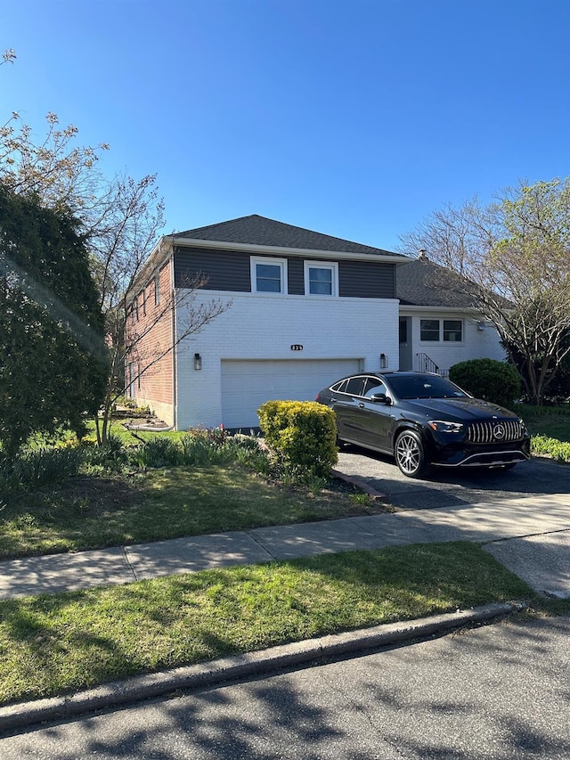 tri-level home with an attached garage, a front yard, and brick siding