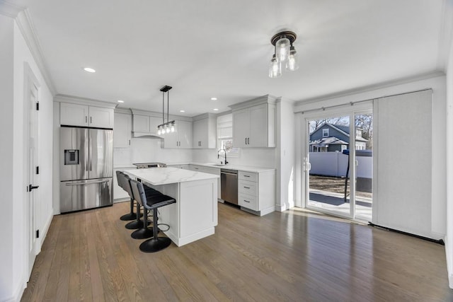 kitchen featuring a breakfast bar area, a kitchen island, dark wood-style flooring, a sink, and appliances with stainless steel finishes