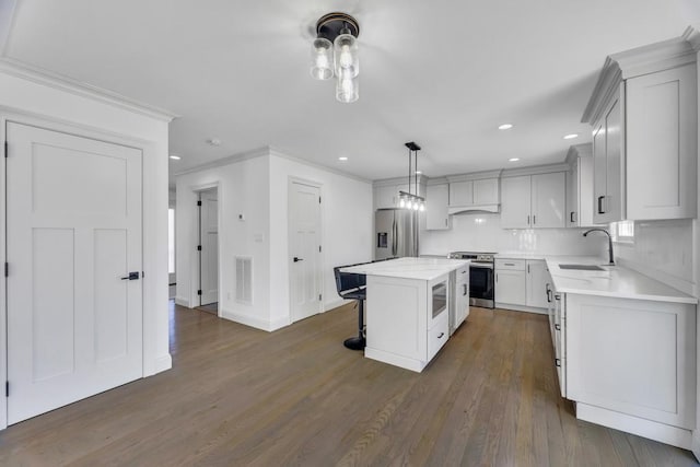 kitchen with a sink, appliances with stainless steel finishes, a breakfast bar area, light countertops, and dark wood-style flooring