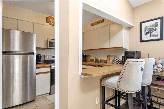 kitchen with cream cabinetry, a kitchen breakfast bar, a peninsula, appliances with stainless steel finishes, and light countertops