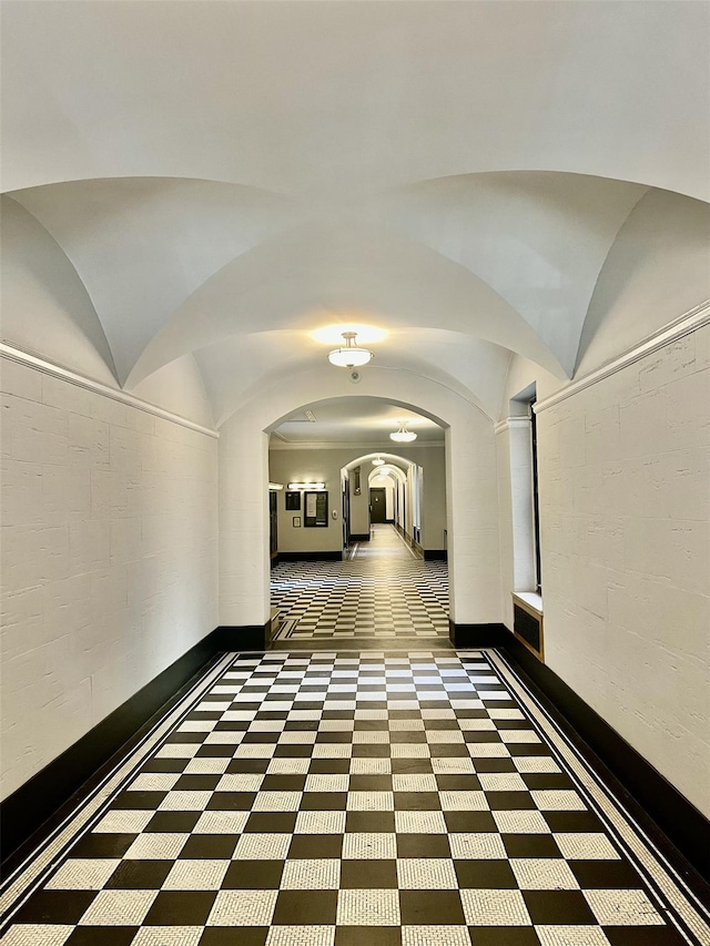 hallway featuring baseboards, arched walkways, and vaulted ceiling