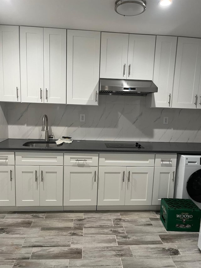 kitchen featuring dark countertops, under cabinet range hood, white cabinetry, and washer / dryer