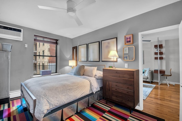 bedroom featuring a wall mounted air conditioner, a ceiling fan, a baseboard heating unit, wood finished floors, and baseboards