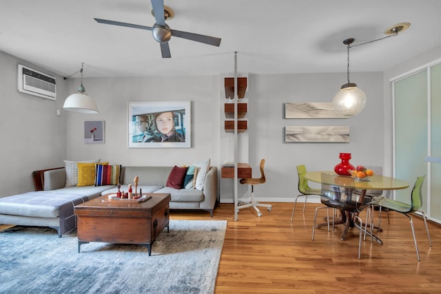 living room with ceiling fan, a wall mounted AC, baseboards, and wood finished floors