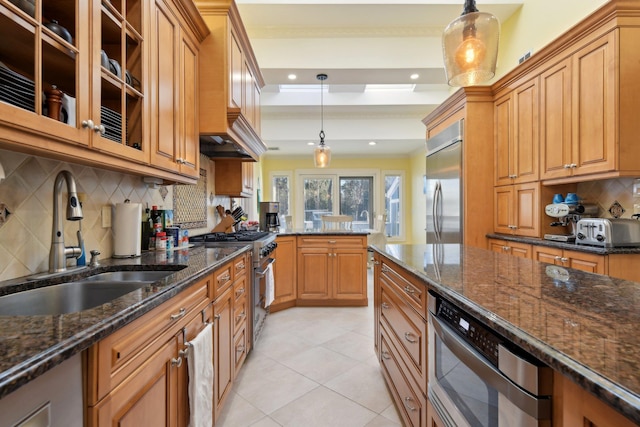 kitchen with brown cabinets, appliances with stainless steel finishes, dark stone counters, and a sink