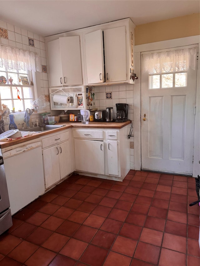 kitchen featuring dark tile patterned flooring, a sink, white cabinets, dishwasher, and tasteful backsplash