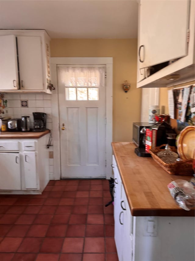 kitchen with decorative backsplash, dark tile patterned floors, butcher block counters, and white cabinetry