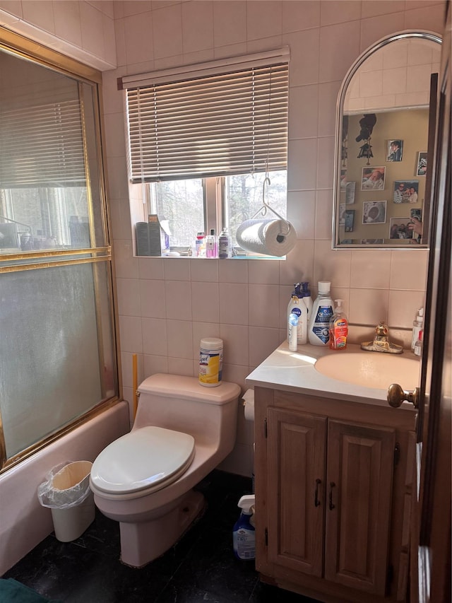 bathroom featuring combined bath / shower with glass door, toilet, tile walls, and vanity