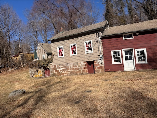 rear view of house featuring a lawn and a shingled roof