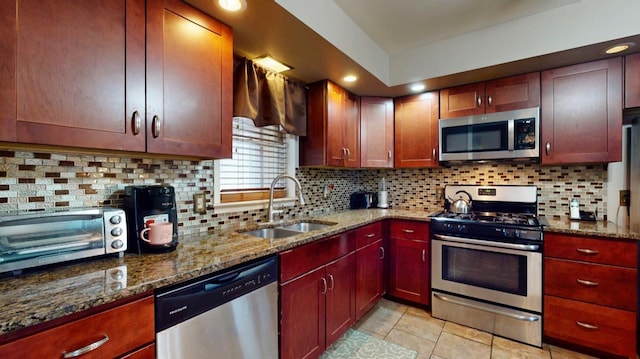 kitchen with backsplash, a toaster, dark stone counters, appliances with stainless steel finishes, and a sink