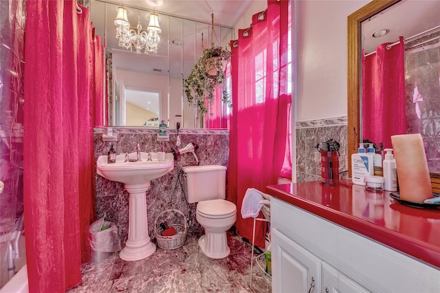 full bath with a chandelier, wainscoting, tile walls, and toilet