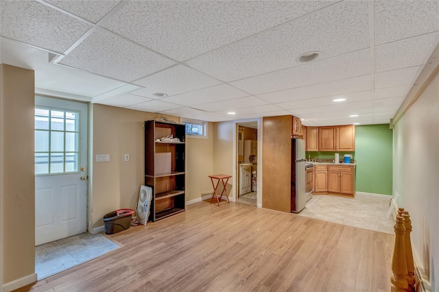 interior space featuring a drop ceiling, light wood-type flooring, freestanding refrigerator, and baseboards